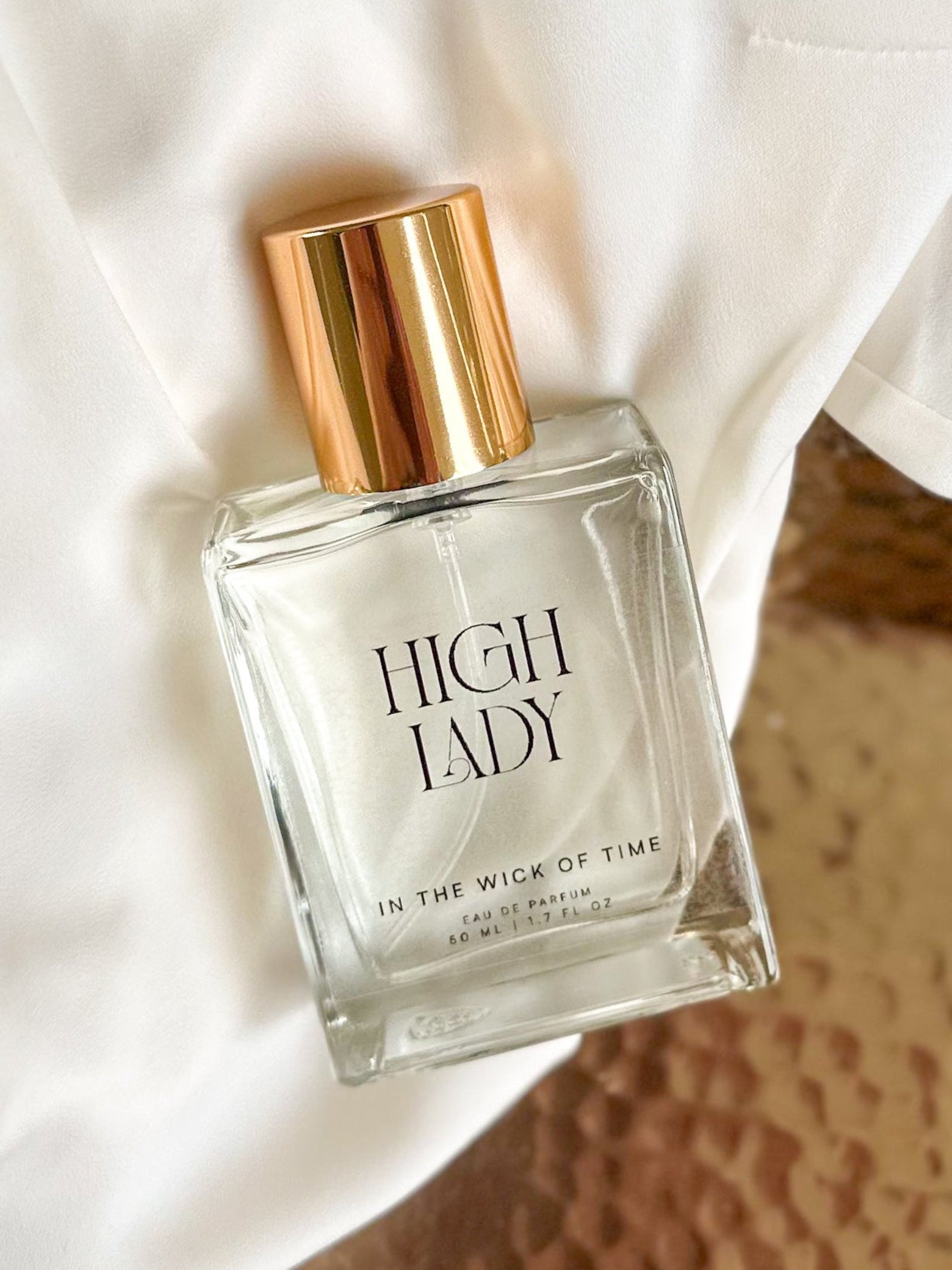 Perfume bottle labeled 'High Lady' on a textured surface with white fabric in the background
